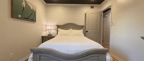 Una habitación de hotel con una cama, una mesita de noche, un ventilador de techo y una puerta.