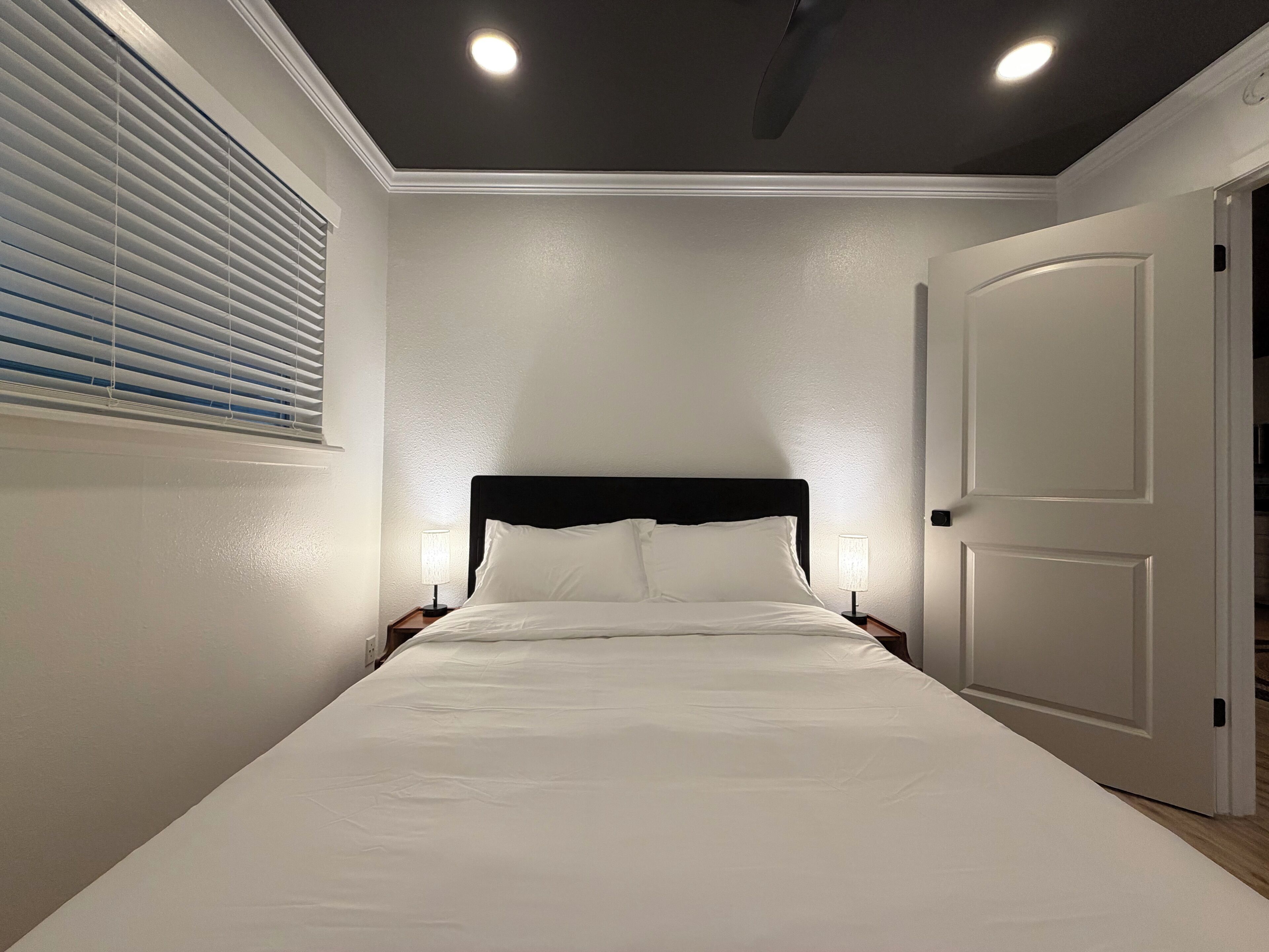 Een slaapkamer met een bed, nachtlampen, een deur en een plafondlamp.