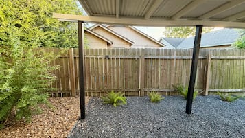 A covered outdoor area with a wooden fence, gravel ground, and a metal roof structure.