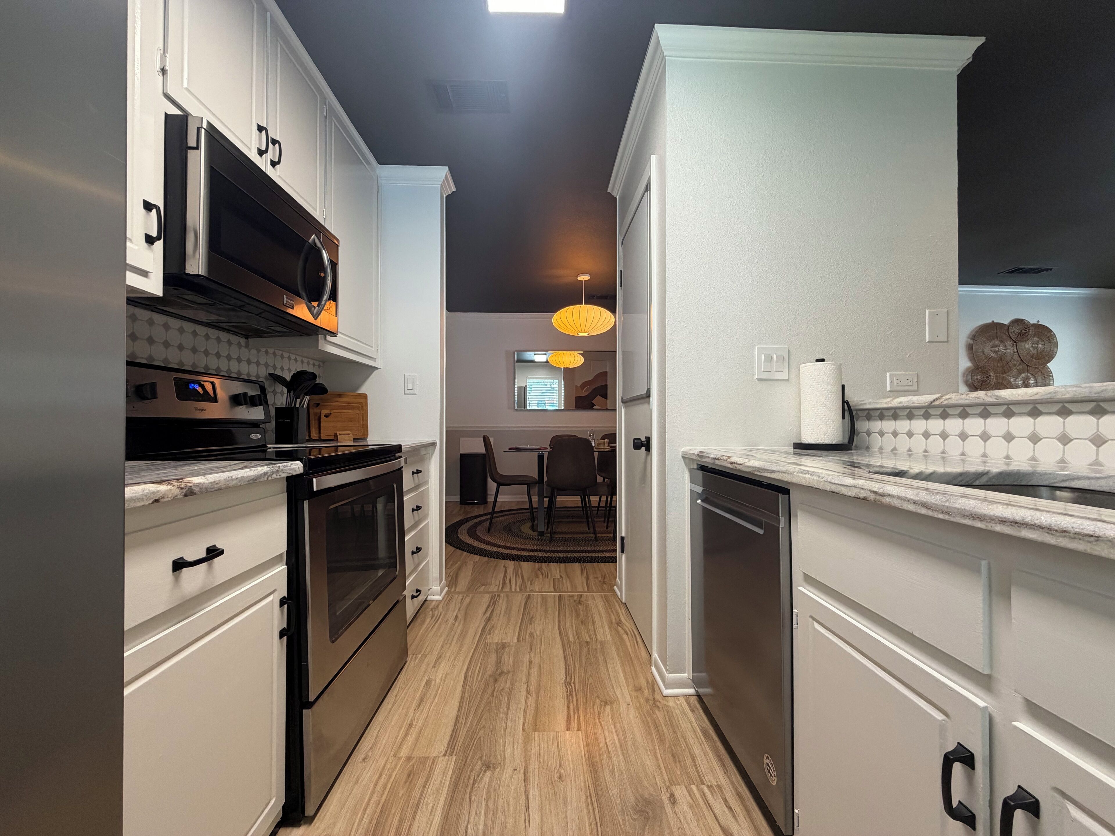 A modern kitchen with stainless steel appliances, wooden flooring, and a view into the dining area.