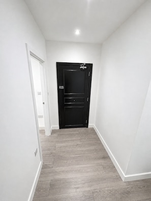 A hallway with a black door, white walls, and wooden flooring. - Luxury 2 Bed Serviced Apt 01 with Wi-Fi MyRent2Rent (Corby)