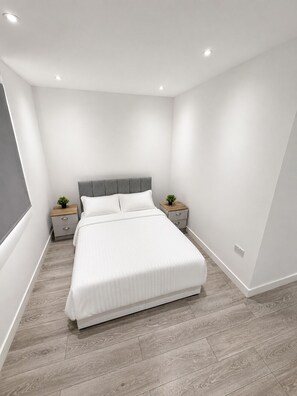 Ein modernes Schlafzimmer mit einem großen Bett, zwei Nachttischen und einem grauen Kopfteil.