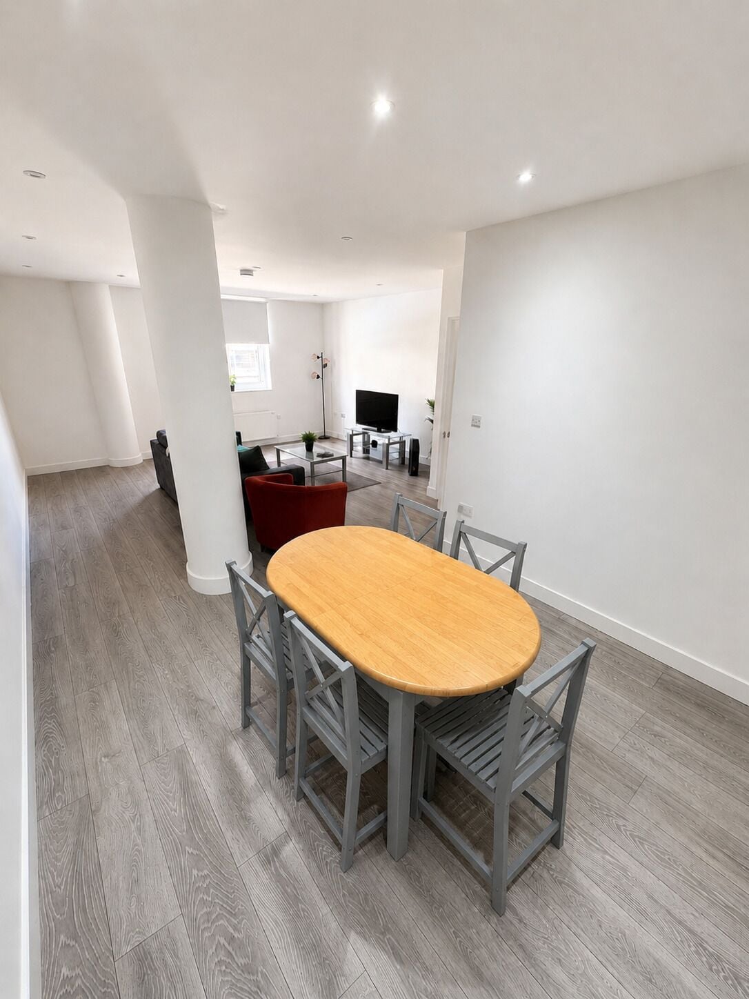 Een moderne woonkamer met een houten eettafel, grijze stoelen, een rode bank en een flatscreen-tv.