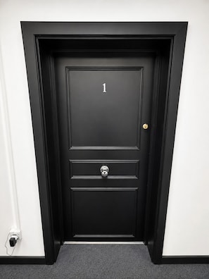 Eine schwarze Tür mit der Nummer 1, einem Schlüsselloch und einem Klingel.