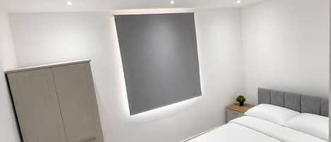 A modern bedroom with a bed, a wardrobe, a bedside table, and a window.