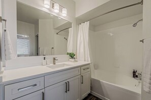 Casa de banho com lavatório branco, espelho e chuveiro.