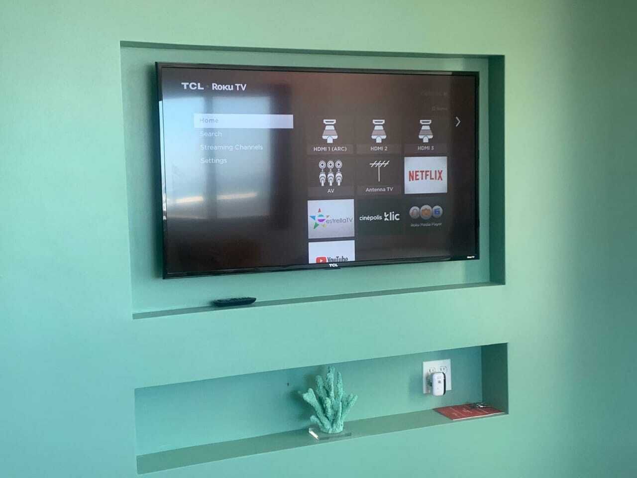 Een TCL Roku televisie bevestigd aan een wand in de kleur turquoise, met een menu-interface.