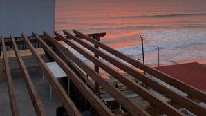 Eine Holzterrasse mit Blick auf einen Strand bei Sonnenuntergang.