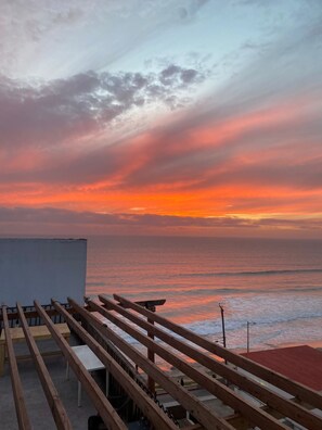 Terraza de madera con vista a una playa y un atardecer.
