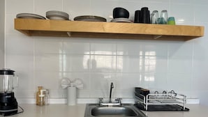 Eine Küche mit einem Holzbodenregal mit Tellern, Schüsseln, einem Mixer, einer Seifenspender und einem Geschirrgestell.