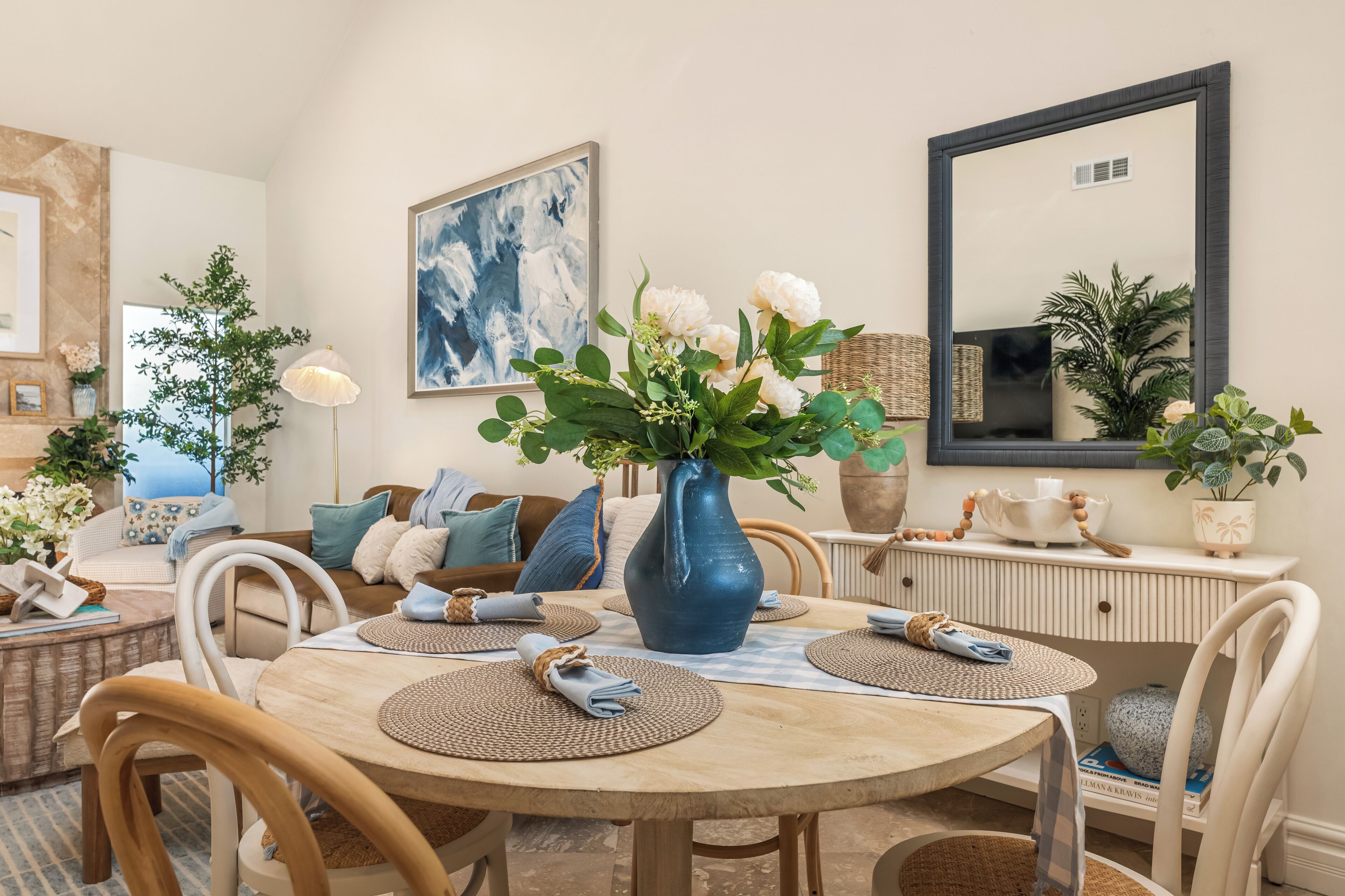 A dining area with a round wooden table, woven placemats, and a blue vase with flowers.