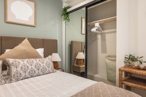 Une chambre à coucher avec un lit, des oreillers, des lampes de chevet, un miroir, une plante et une armoire.