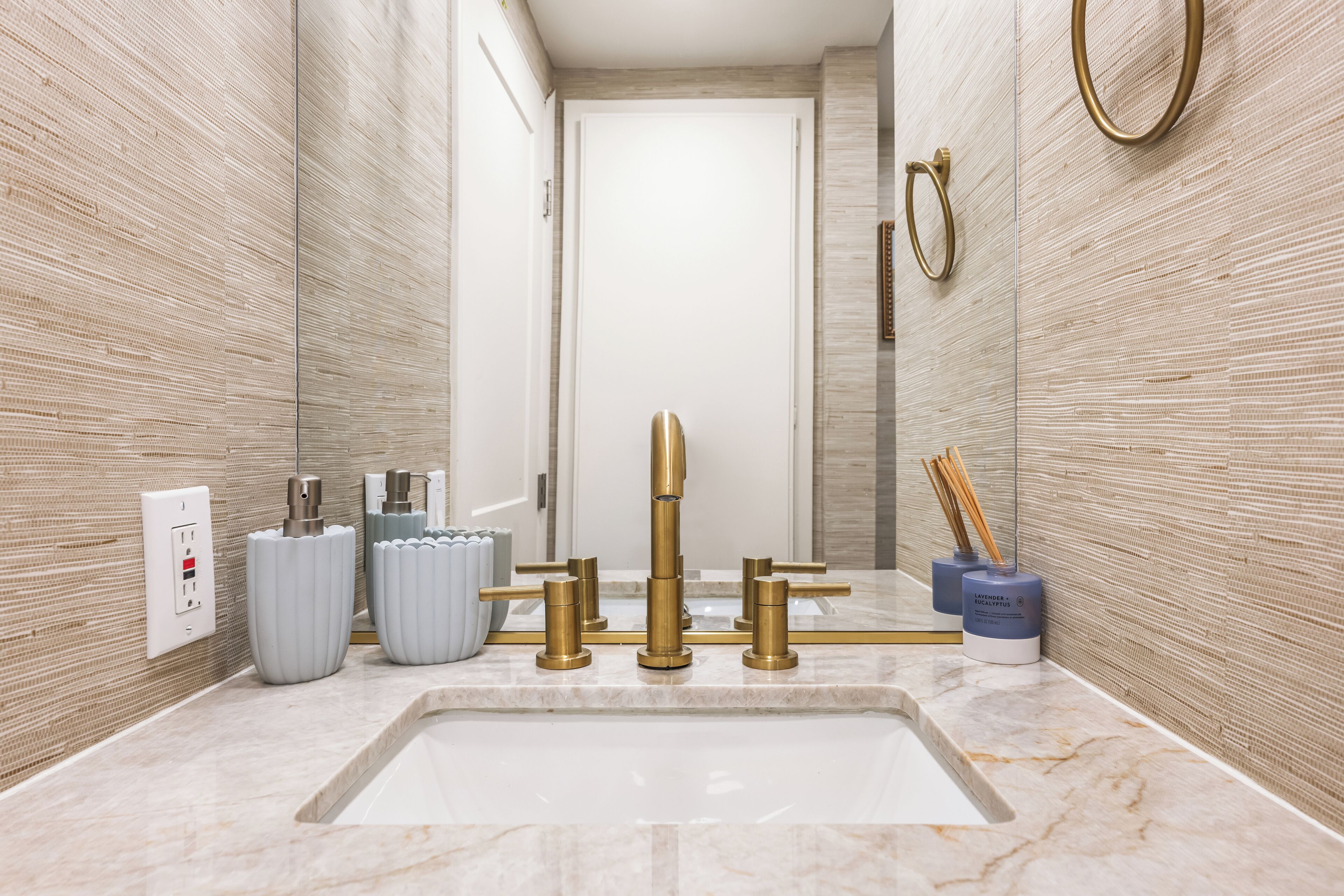 A modern bathroom with a marble sink, gold fixtures, and a textured wall.