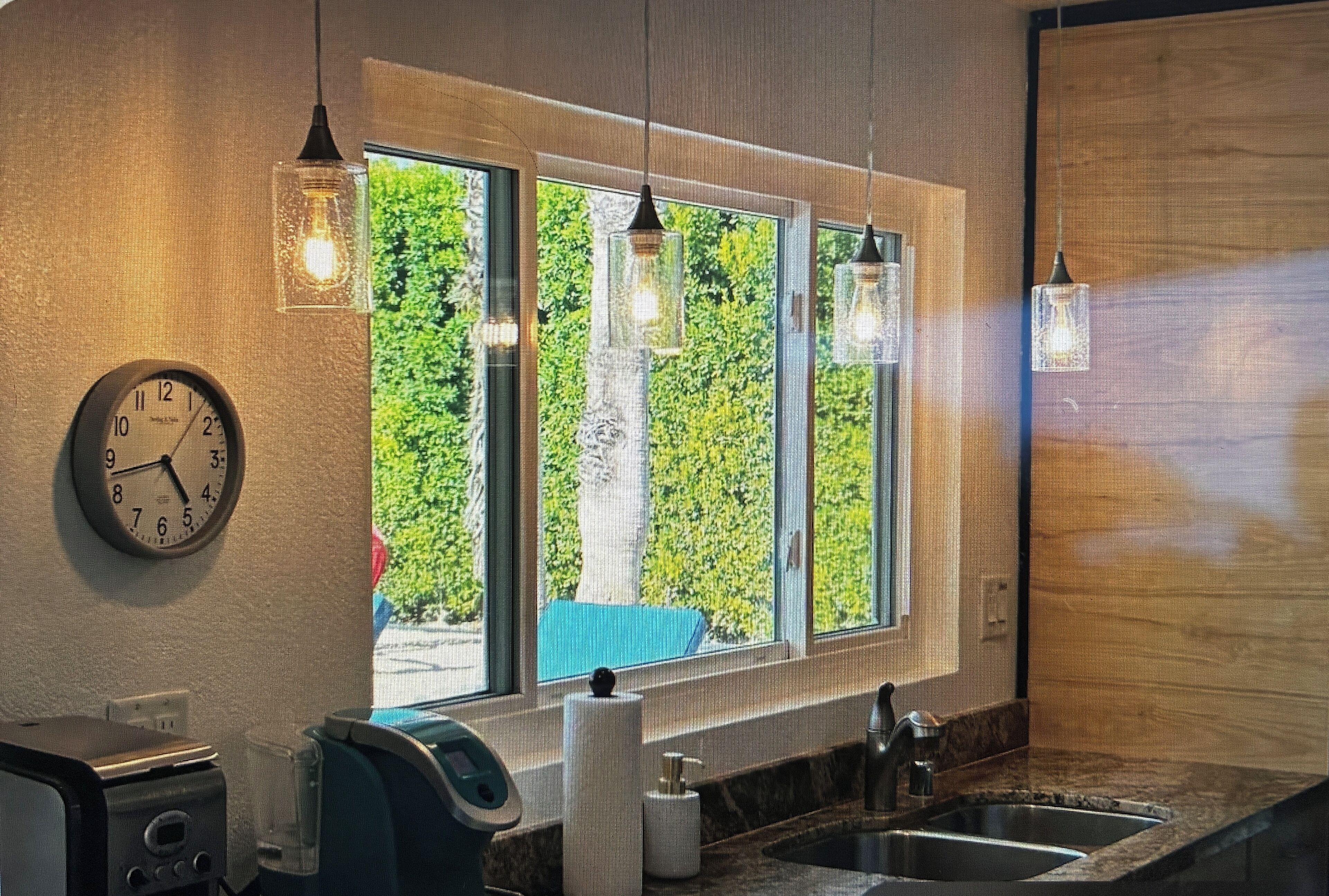 Une salle de bain avec une horloge, une fenêtre donnant sur un paysage verdoyant et un lavabo.