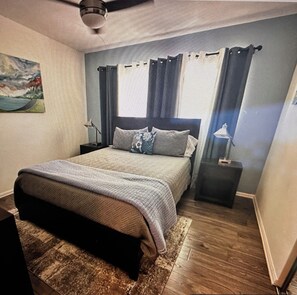 Une chambre à coucher avec un lit, des tables de chevet, un ventilateur de plafond et une fenêtre avec des rideaux.