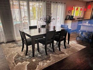 Un coin repas avec une table et des chaises, un vase avec des plantes et, au fond, une cuisine.