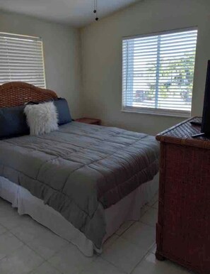 A bedroom with a bed, a nightstand, a television, and a window with blinds.
