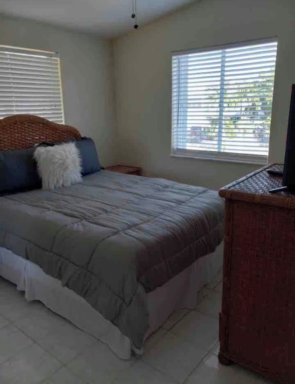 A bedroom with a bed, a nightstand, a television, and a window with blinds.