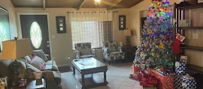 A living room with a coffee table, two armchairs, a sofa, a Christmas tree, and a fireplace.