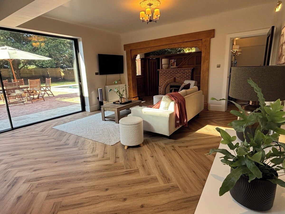 A modern living room with a fireplace, a sofa, a coffee table, and a large window overlooking a patio area.