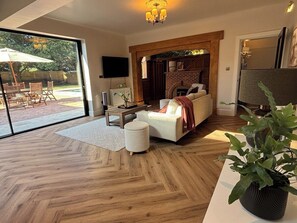 A modern living room with a fireplace, a sofa, a coffee table, and a large window overlooking a patio area. - Family beach escape with Pool (Bournemouth)