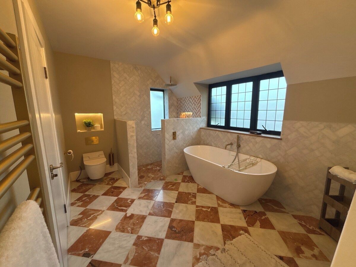 A bathroom with a freestanding bathtub, a toilet, a shower area, and a window providing natural light.