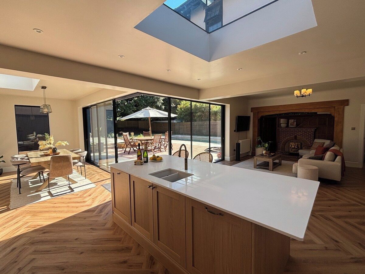 A modern kitchen with a large island, wooden cabinets, and a skylight.