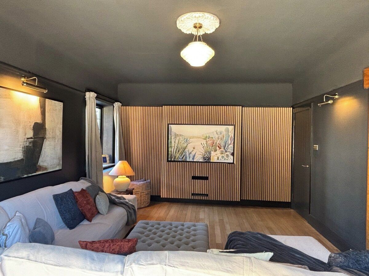Ein modernes Wohnzimmer mit einer Couch, einem Hocker und einem Flachbildfernseher, der an einer Wand aus Holzpaneelen befestigt ist.