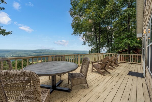 Een houten terras met een ronde tafel en rieten stoelen, met uitzicht op een prachtig landschap.