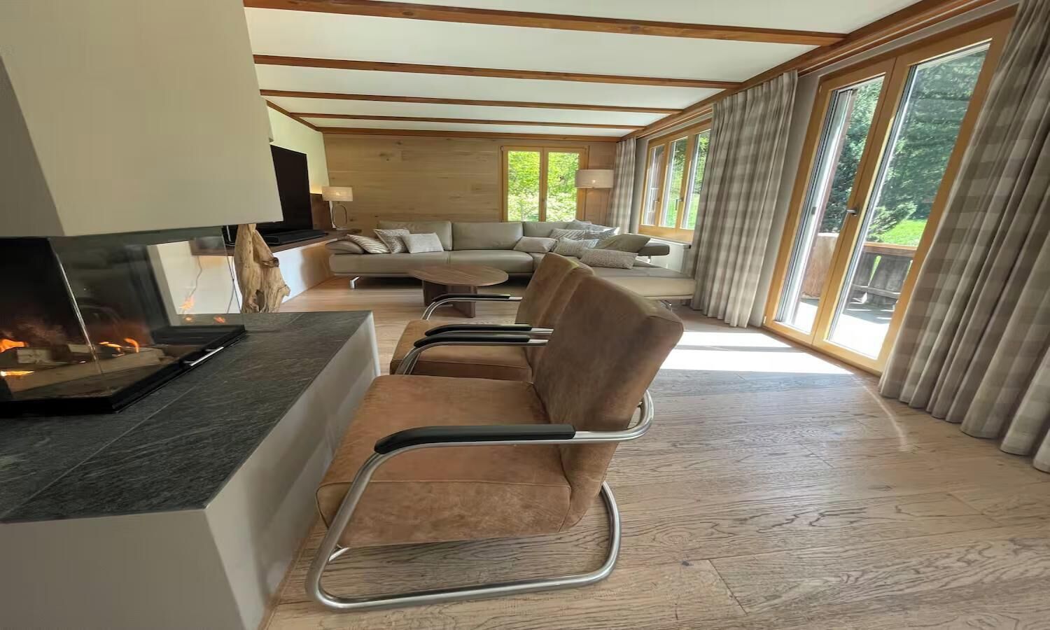 A modern living room with a fireplace, comfortable seating, and large windows.