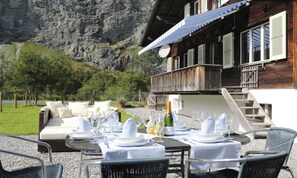 An outdoor dining area with tables set for a meal, overlooking a mountainous landscape.