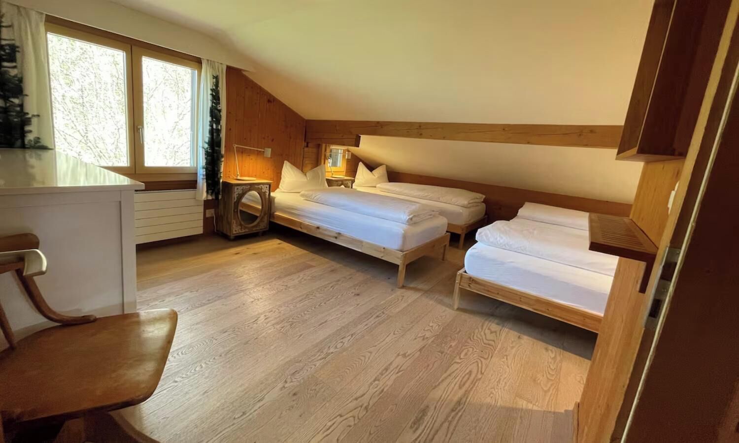 Ein gemütliches Zimmer mit Holzboden, einem Bett, einem Schreibtisch und einem Stuhl.