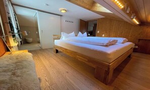 A wooden-framed bed with white bedding in a room with wooden walls and floors.