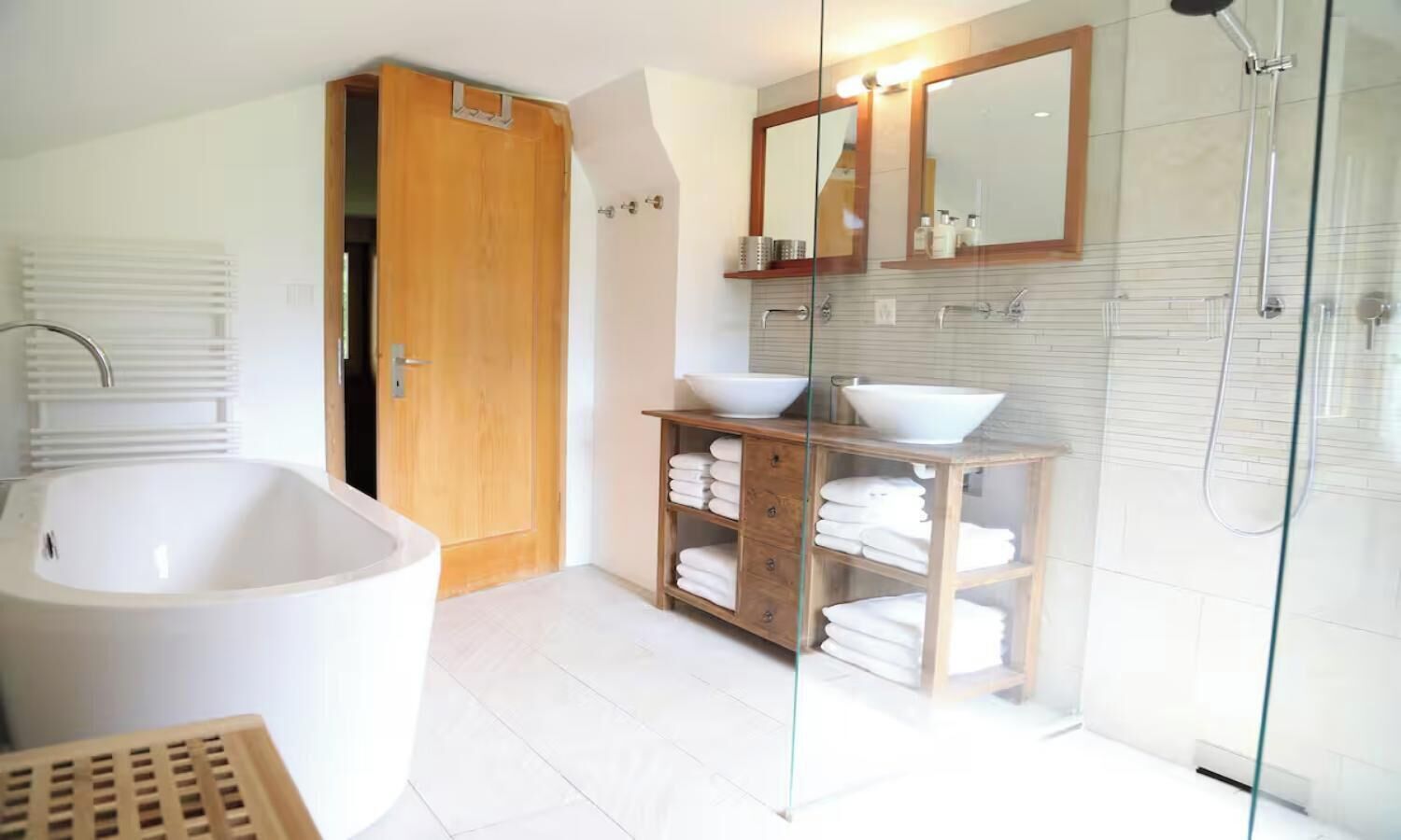 A modern bathroom with a freestanding bathtub, a glass-enclosed shower, and a vanity with a mirror and two sinks.