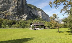 A chalet with a sloped roof, surrounded by a well-maintained lawn and a mountain backdrop.