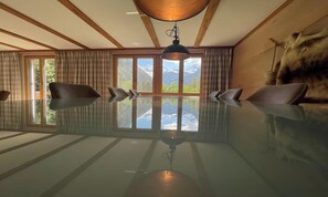 A room with a large glass table, wooden beams on the ceiling, and a view of mountains through large windows.