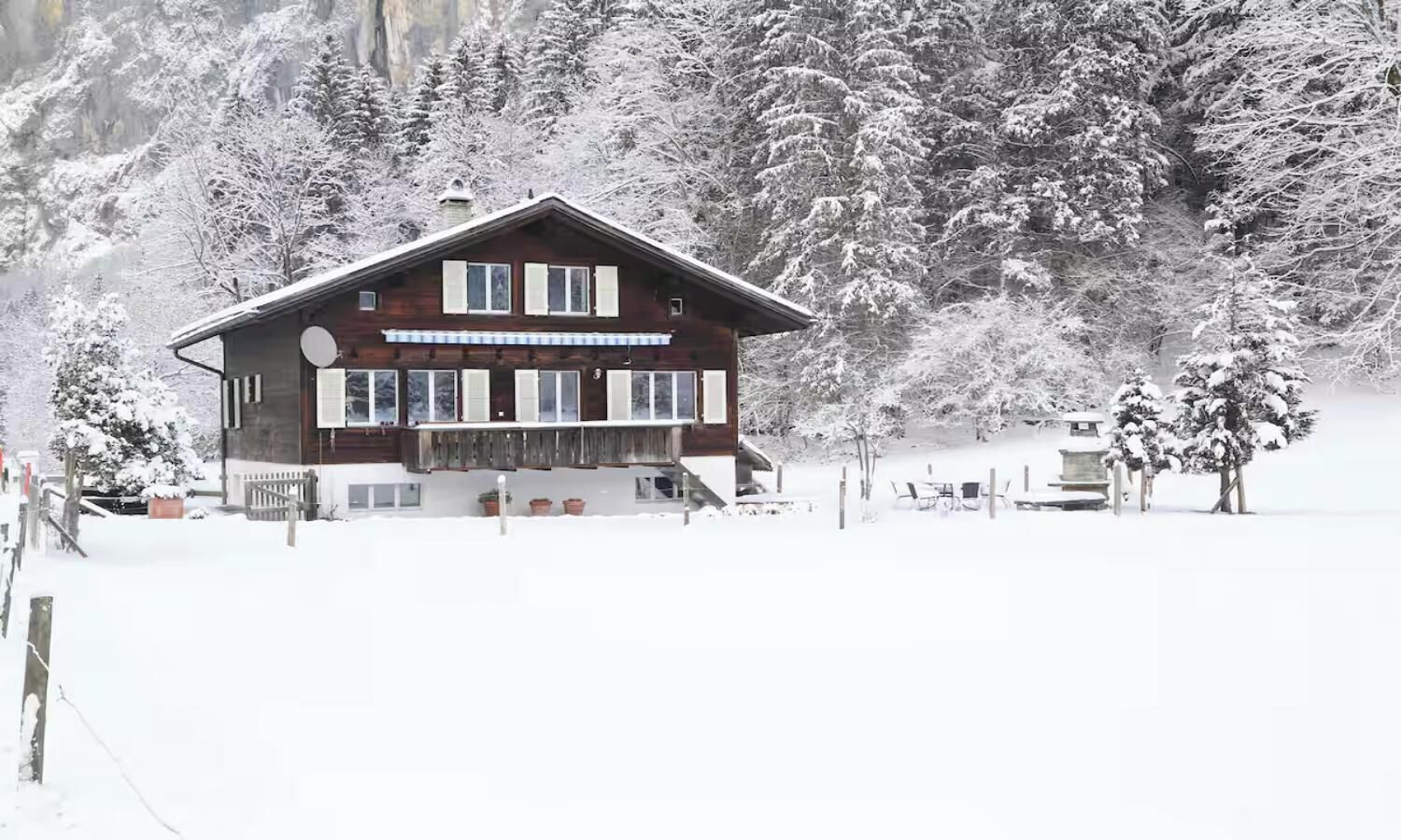 A wooden chalet with a balcony, surrounded by snow-covered trees and a clear sky.