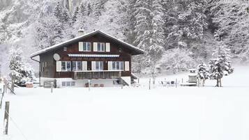 A wooden chalet with a balcony, surrounded by snow-covered trees and a clear sky.