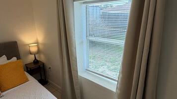 Quarto de hotel com cama, mesa de cabeceira com luminária, janela com cortinas e vista para o exterior.