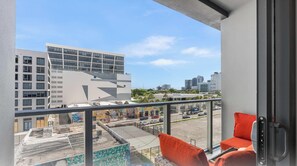 Ein Balkon mit Blick auf eine Stadtansicht, darunter moderne Gebäude und ein Parkplatz.
