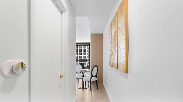 A hallway with a white door, a dining area with a table and chairs, and a view of a building through a window.
