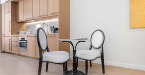 A modern kitchen with wooden cabinets, a built-in oven, and a dining area with two upholstered chairs and a small table.