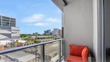 Un balcon donnant sur une vue panoramique de la ville, une chaise rouge et un bâtiment orné d’une fresque colorée.