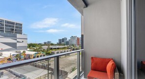 Uma varanda com vista para o horizonte urbano, uma cadeira vermelha e um edifício com um mural colorido.