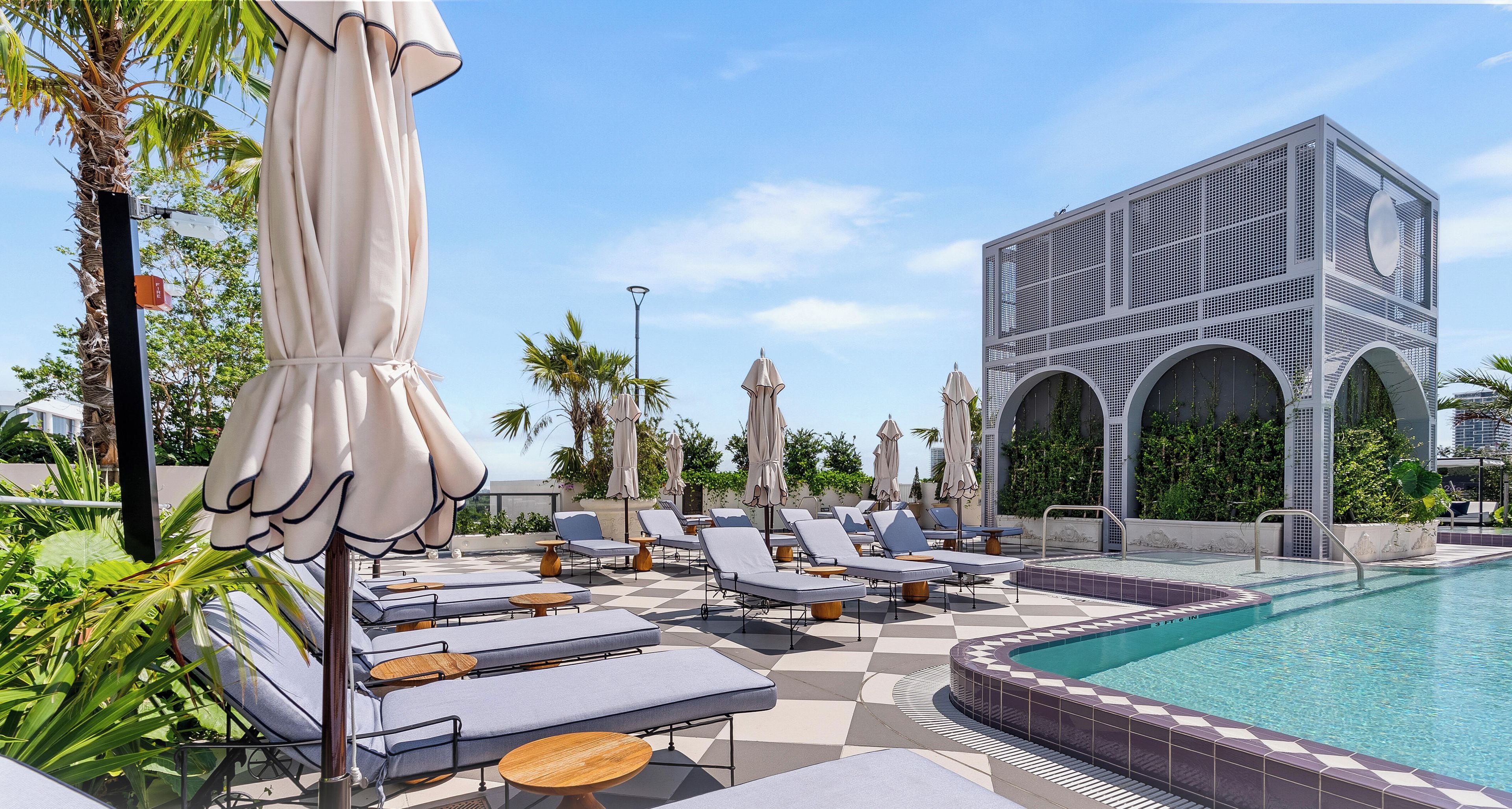 A poolside area with lounge chairs and umbrellas, a pool with a tiled edge, and a modern building with arches.