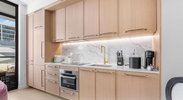 Uma cozinha moderna com armários de madeira, forno Bosch, pia com torneira dourada e máquina de café.