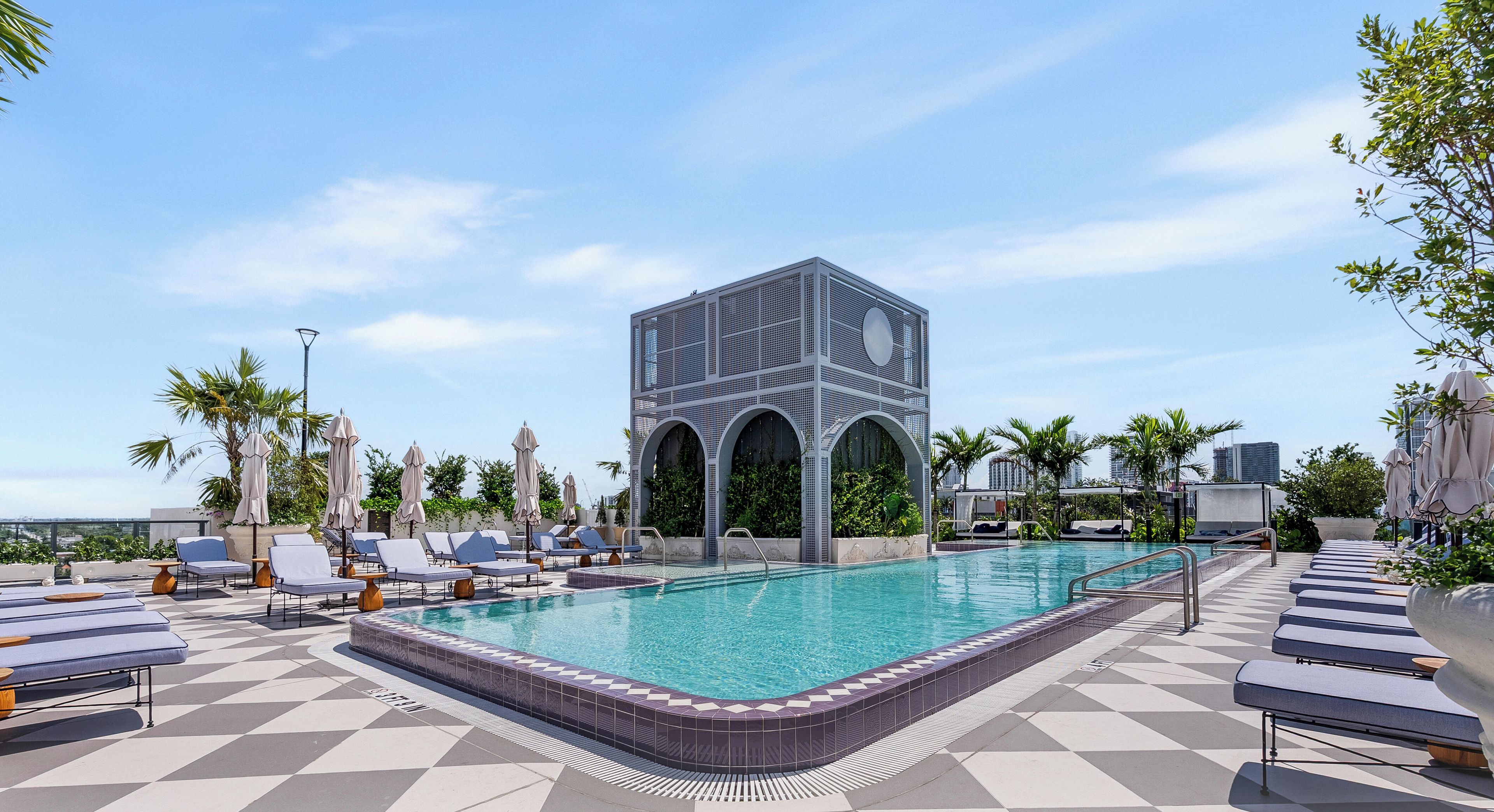 Área de piscina no terraço com espreguiçadeiras, piscina e uma estrutura de prédio moderna.