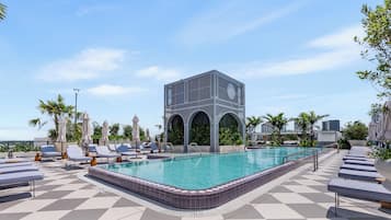 Área de piscina no terraço com espreguiçadeiras, piscina e uma estrutura de prédio moderna.