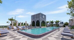 Área de piscina no terraço com espreguiçadeiras, piscina e uma estrutura de prédio moderna.