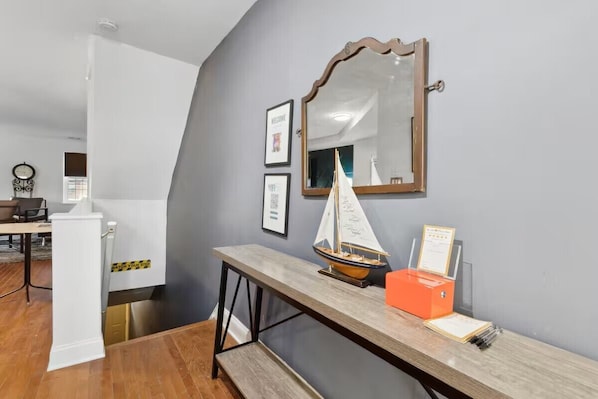 A room with a desk, a small sailboat model, a mirror, and a framed welcome sign.